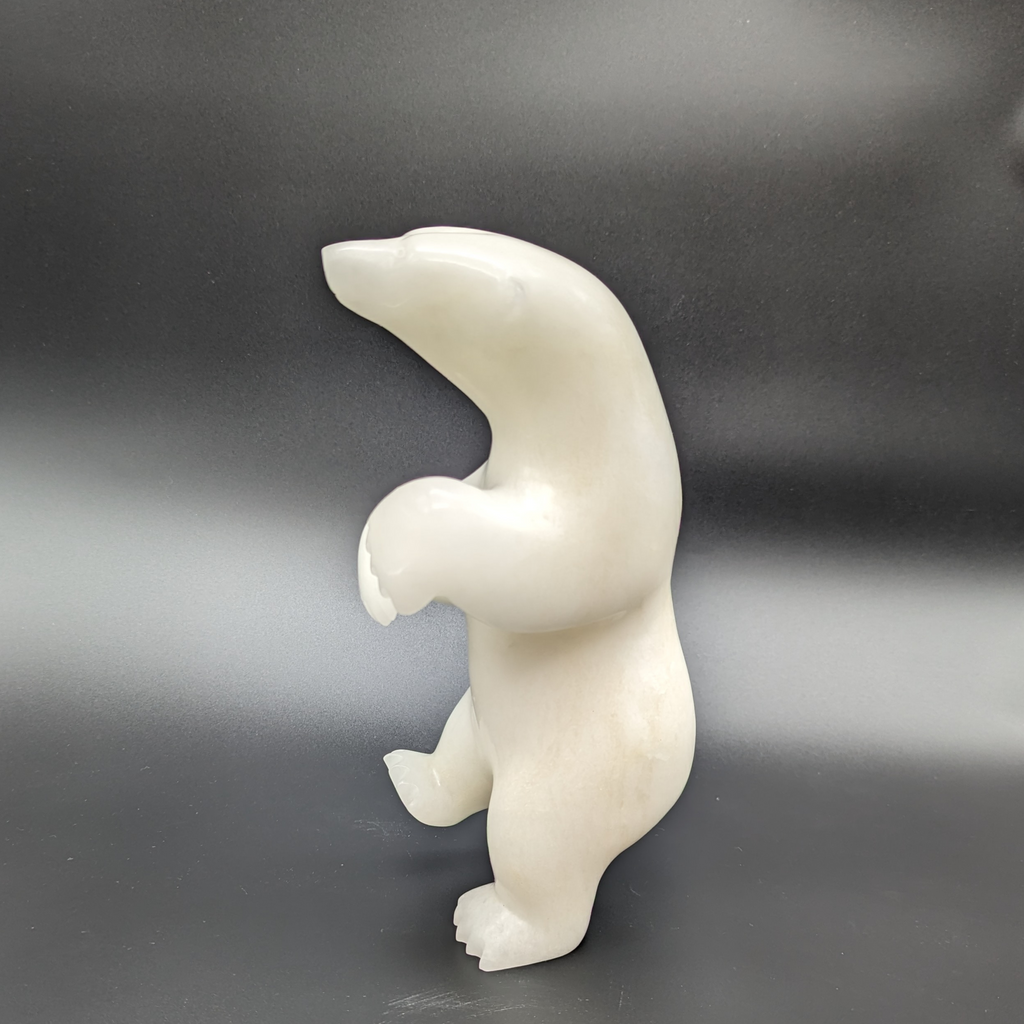 A dancing bear carved from white alabaster. The bear dances on one foot, with the other hind foot raised and its paws in front of it. This bear faces left.