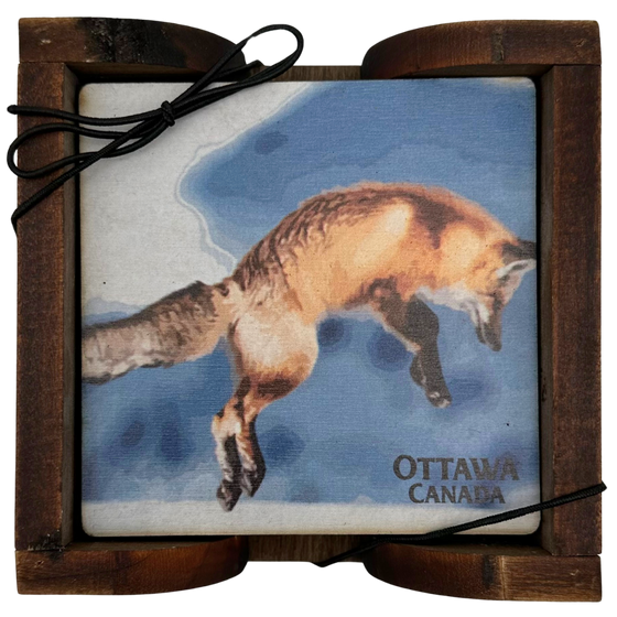 A square wooden coaster displayed in an attractive wooden holder. The coaster shows a leaping red fox depicted against a blue sky. The coaster says "Ottawa Canada" in the bottom right, beneath the fox.