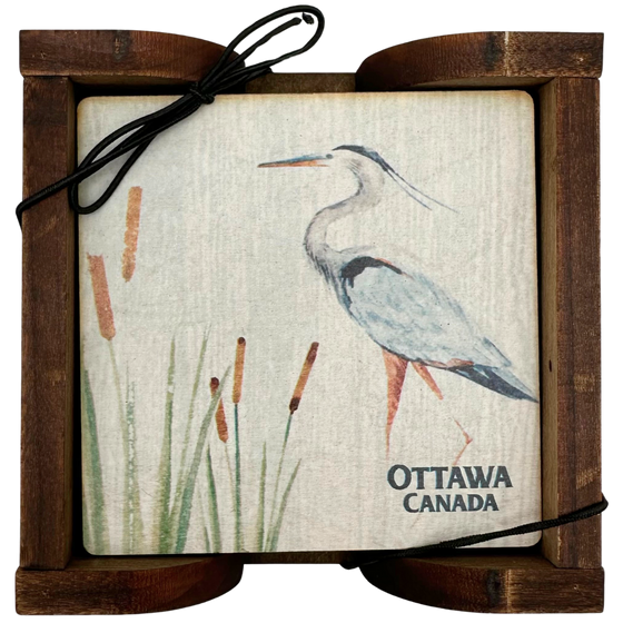 A square wooden coaster contained in an attractive holder. The coaster shows a majestic blue heron standing in reeds against a white background and "Ottawa, Canada" written on the bottom.