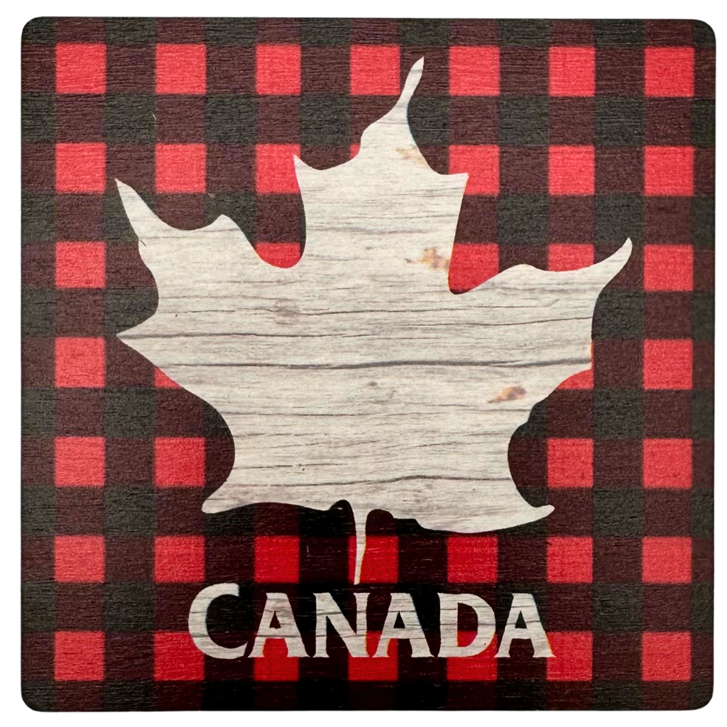 A square wooden coaster with a maple leaf in distressed wood against a background of red and black plaid. Below the maple leaf, the coaster says "Canada"