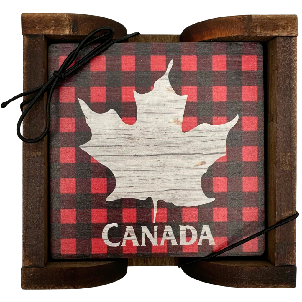 A square wooden coaster displayed in an attractive wooden holder. The coaster shows a maple leaf in distressed wood against a background of red and black plaid. Below the maple leaf, the coaster says "Canada"