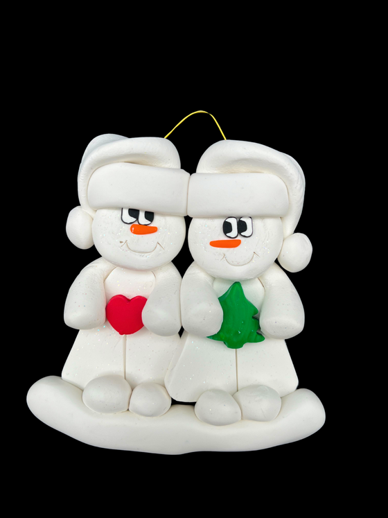 Two smiling snowmen in white hats gaze at each other. The left one holds a heart and the right holds a Christmas tree.