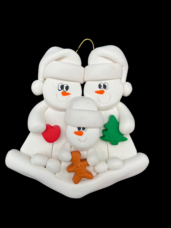 Two smiling snowmen in white hats gaze at each other. The left one holds a heart and the right holds a Christmas tree. In front of them, a smaller snowman holds a gingerbread man.