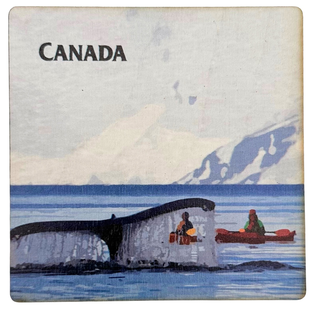 A square wooden coaster with a whale fluke about to slap the water. Two people in kayaks observe in the midground, with a mountain in the background. The coaster says "Canada" in the top left corner.