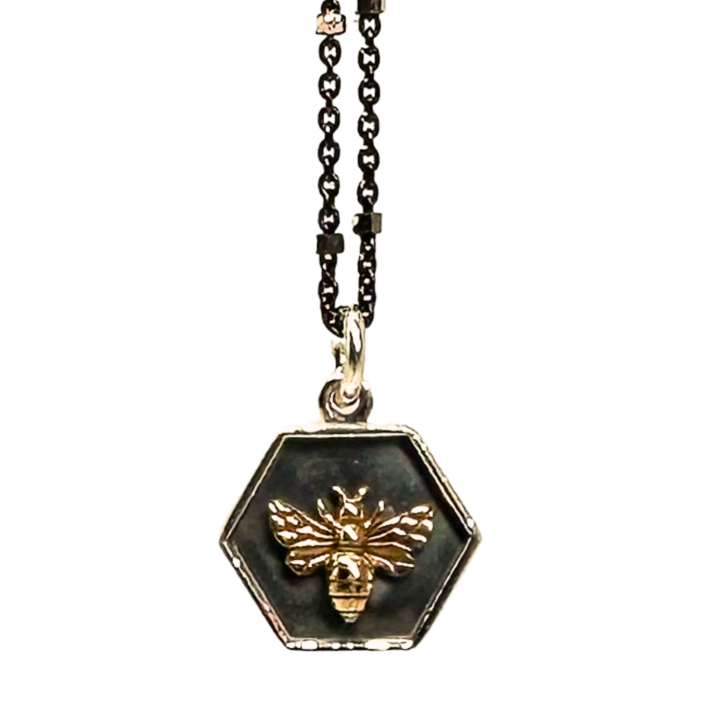 Black chain with thin hexagonal silver rings that are evenly distributed throughout the chain. Silver hexagonal pendent with a grey background. The silver edges of the pendent are lifted and in the center of the hexagon there is a gold bumblebee. 