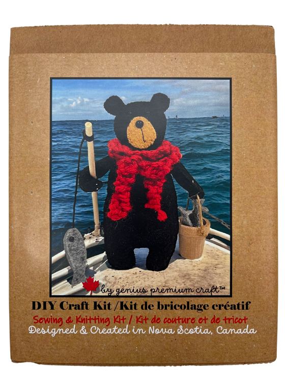 A handmade felted black bear stands holding a fishing rod, complete with felt fish, in one hand, and a bucket with more fish in the other. The bear wears a chunky knitted red scarf.