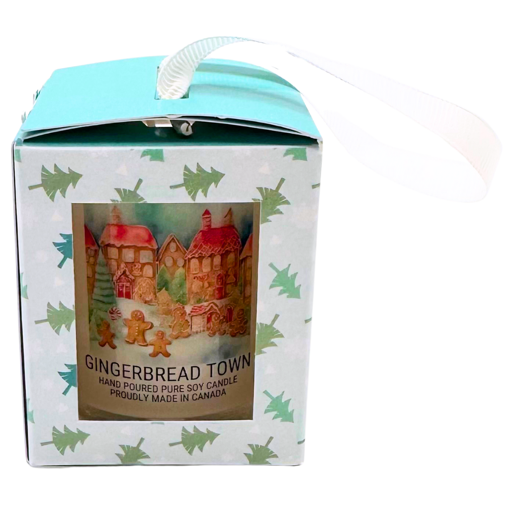 A candle with a gingerbread town inside a light blue box with small green christmas trees on it. Has a white handle.