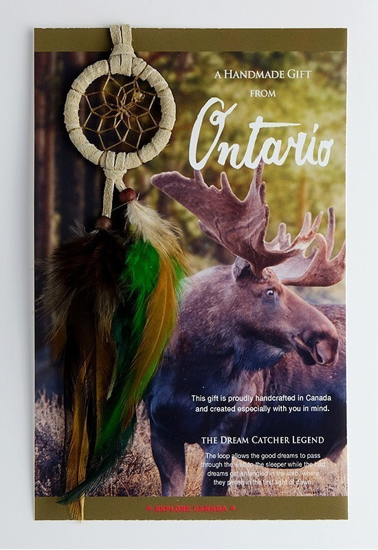 A mini dream catcher in natural tones with earthy brown and green feathers and brown beads and stones decorating the piece. The card attached to it depicts a majestic Canadian moose in the wilderness and the text "A Handmade Gift from Ontario."