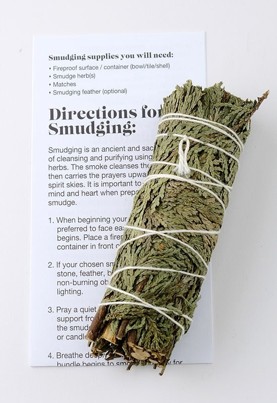 A traditional cedar smudge bundle, used for smudging ceremonies. The bundle sits on step-by-step directions for a successful smudging ceremony, also included.