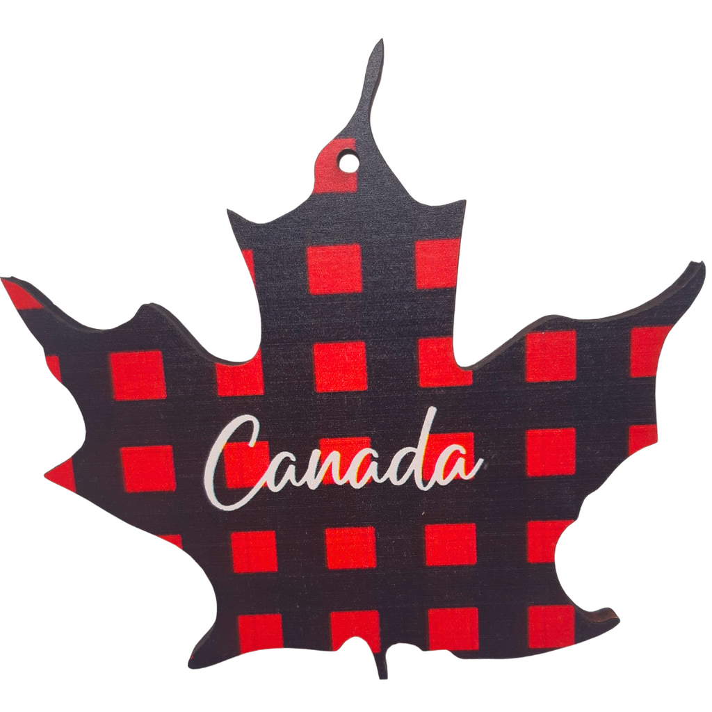 The ornament is entirely plaid and shaped like a maple leaf. In the middle reads "Canada" in white script.