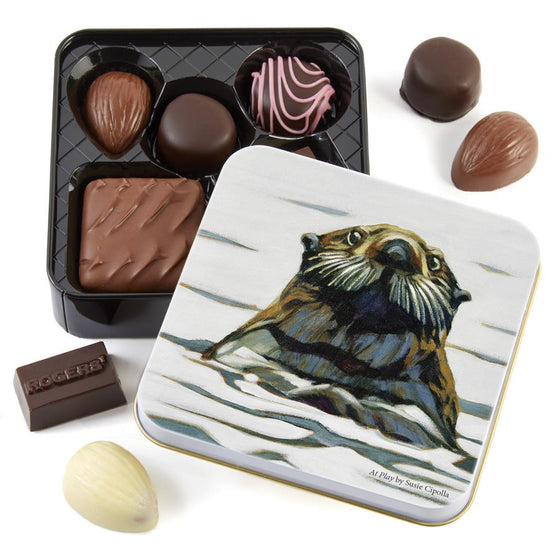 Delicious assorted chocolates in a stylish tin. On the cover of the tin, a beautiful otter looks at the viewer as it bobs in the waves.