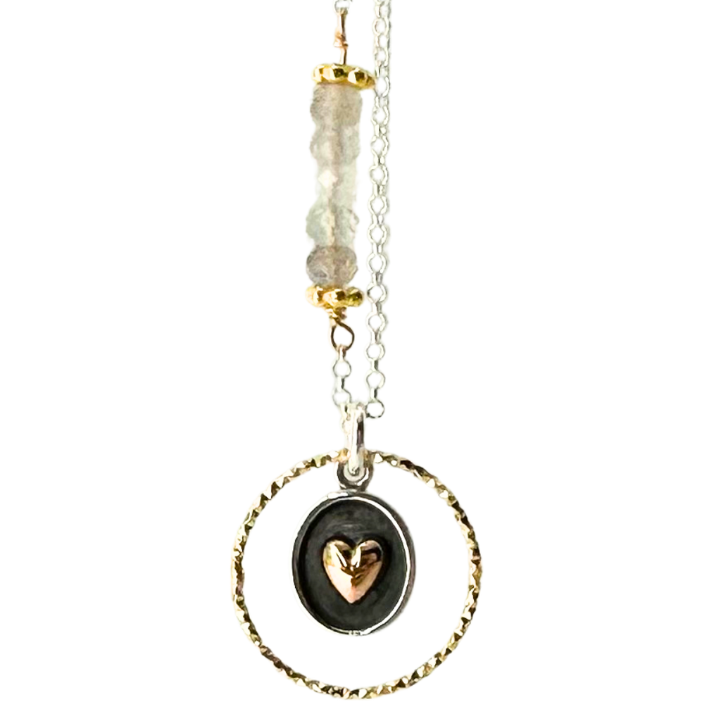 Silver chain with 5 coloured beads in middle of chain attached with gold chain links that look like flowers. Pendent is a gold ring that has triangle ridges. Inside of gold rind is an oval with a silver outline and grey background. There is a gold heart in the center. 