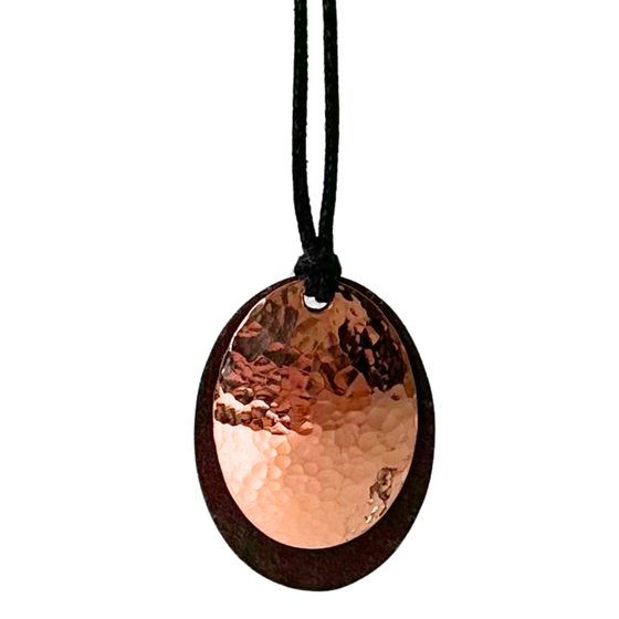 A beautiful necklace made of copper and tin mounted on a leather cord. The pendant is made of two layers: antique upcycled tin cut into an oval forms the base, and then a hammered copper circle is overlaid to create stunning contrast.