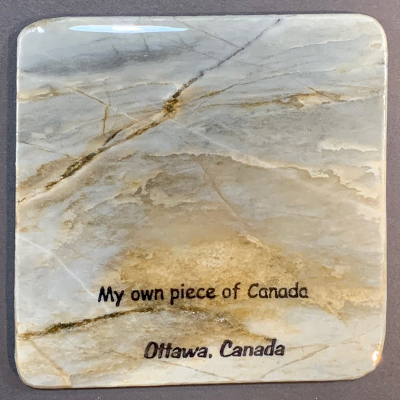 This coaster is made of a piece of Canadian Shield marble with mineral lines running through in unique colours, lines, and patterns. The words "My Own Piece Of Canada" are printed on the front, with "Ottawa, Canada" below. The coaster is finished with a clear coat, giving it a shiny finish.