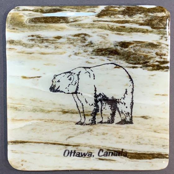 This coaster features the image of the side view of a polar bear with the words Ottawa, Canada below. The image is on a piece of canadian shield marble with mineral lines running through in unique colours, lines, and patterns. The coaster is finished with a clear coat, giving it a shiny finish.